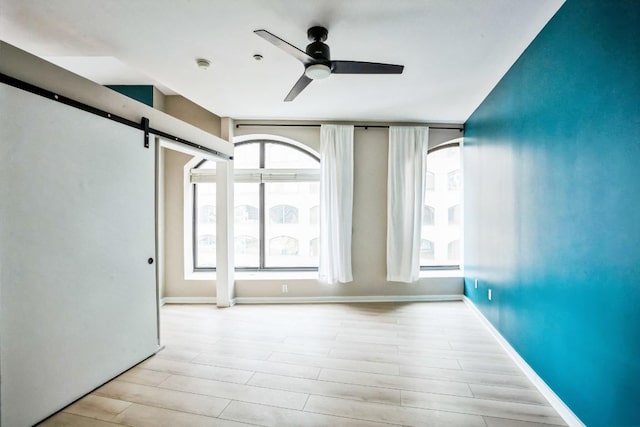 spare room featuring a ceiling fan, wood finished floors, baseboards, and a barn door