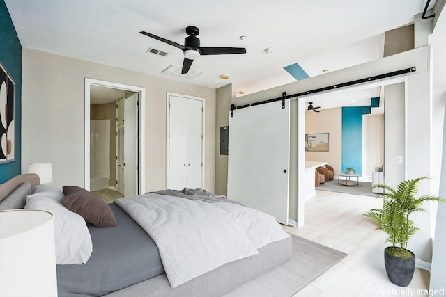 bedroom featuring a barn door, visible vents, a ceiling fan, connected bathroom, and wood finished floors