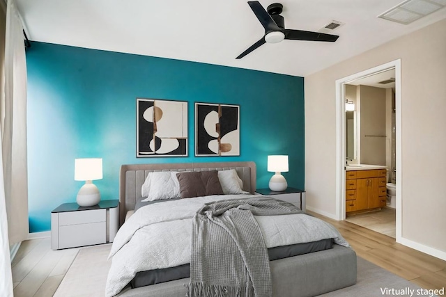 bedroom with light wood-style floors, visible vents, baseboards, and ensuite bathroom