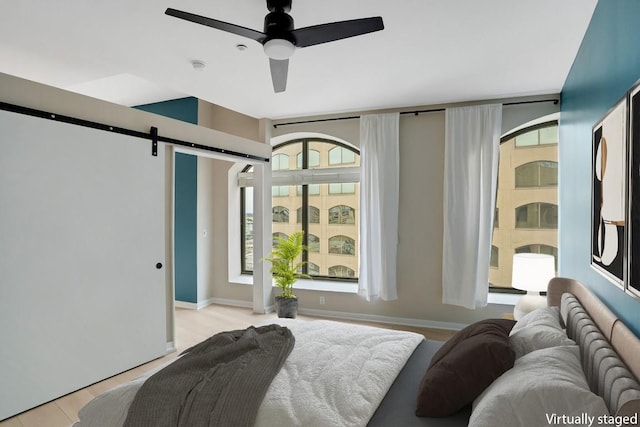 bedroom featuring ceiling fan, a barn door, and baseboards