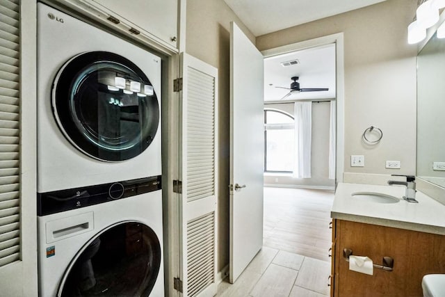 laundry area with laundry area, visible vents, stacked washer / drying machine, light wood-type flooring, and a sink