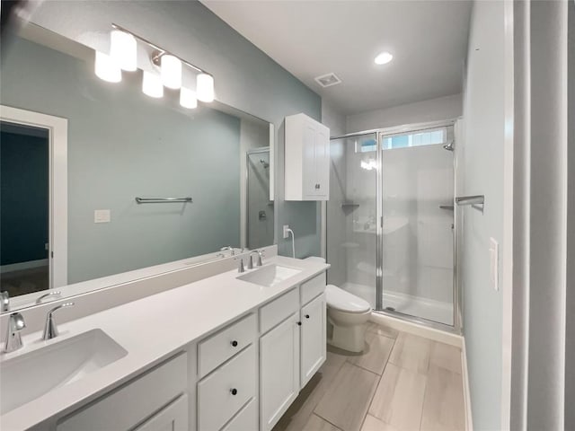 bathroom with toilet, a shower stall, double vanity, and a sink