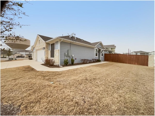 view of side of property featuring a garage, fence, stone siding, a yard, and concrete driveway