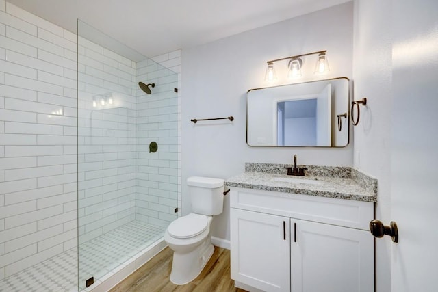 full bathroom with vanity, wood finished floors, a tile shower, and toilet