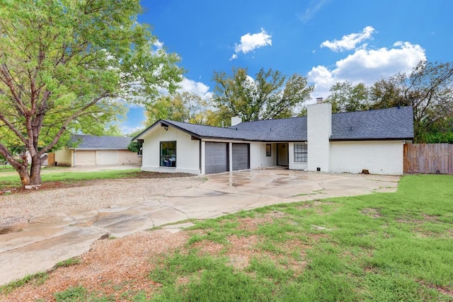 rear view of house with a garage, fence, driveway, a lawn, and a chimney