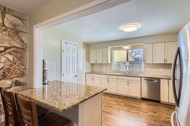 kitchen featuring light stone counters, a peninsula, stainless steel appliances, light wood-type flooring, and a sink