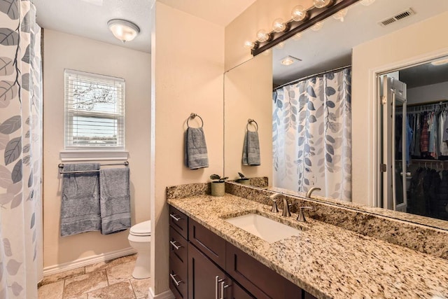 bathroom featuring toilet, vanity, visible vents, and baseboards