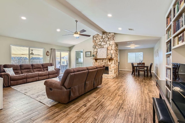 living area featuring lofted ceiling with beams, baseboards, wood finished floors, and a stone fireplace