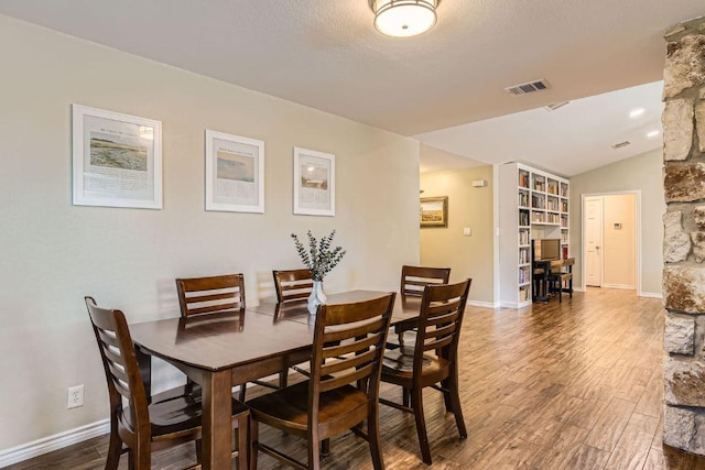 dining room with baseboards, visible vents, lofted ceiling, wood finished floors, and a textured ceiling