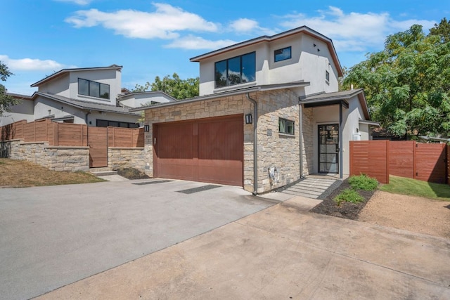 modern home featuring stone siding, driveway, fence, and a gate