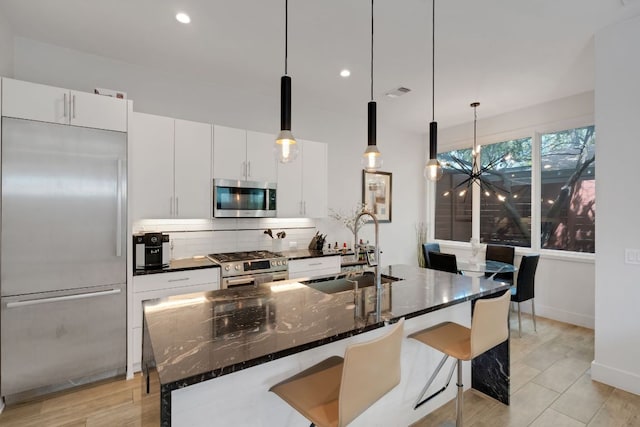 kitchen featuring visible vents, decorative backsplash, appliances with stainless steel finishes, a sink, and an island with sink