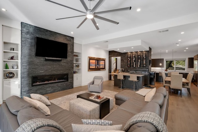 living room featuring built in shelves, indoor wet bar, a fireplace, light wood finished floors, and visible vents