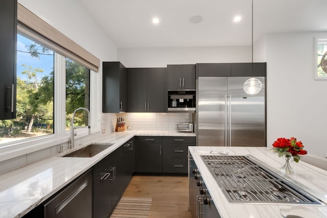 kitchen with stainless steel appliances, light stone countertops, a sink, and tasteful backsplash