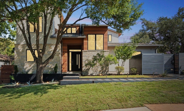 contemporary house with a front yard, stone siding, fence, and stucco siding