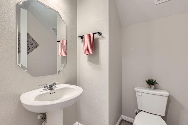 bathroom with vaulted ceiling, toilet, a textured wall, and a sink