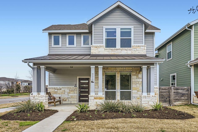 view of front facade featuring a porch, a standing seam roof, metal roof, fence, and stone siding