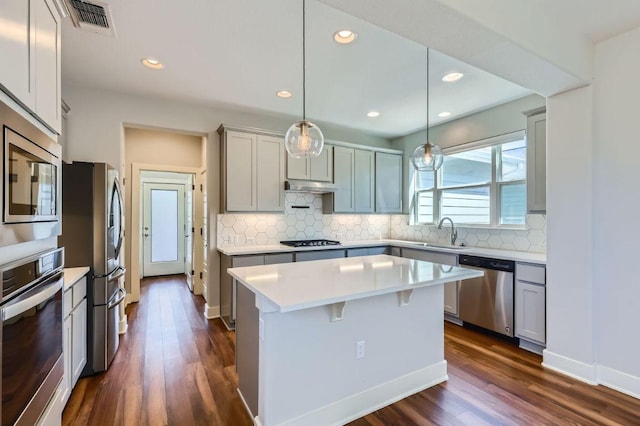 kitchen featuring under cabinet range hood, dark wood-style flooring, a sink, light countertops, and appliances with stainless steel finishes