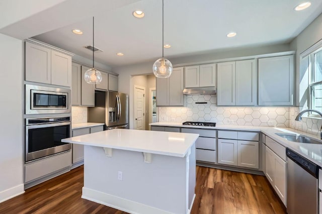 kitchen with light countertops, appliances with stainless steel finishes, a sink, a kitchen island, and under cabinet range hood