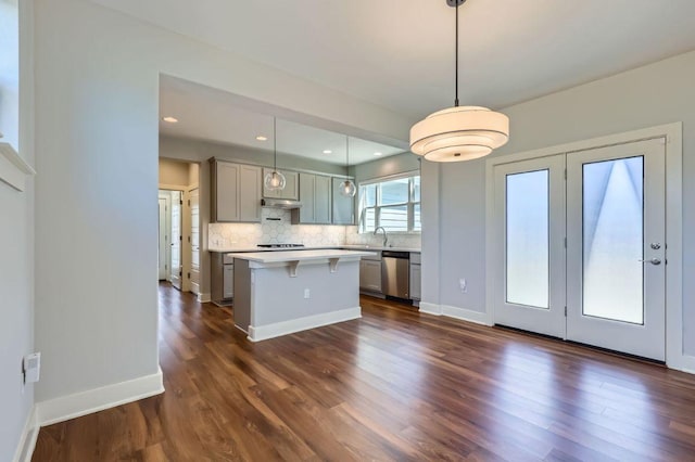 kitchen with a kitchen breakfast bar, light countertops, stainless steel dishwasher, gray cabinets, and tasteful backsplash