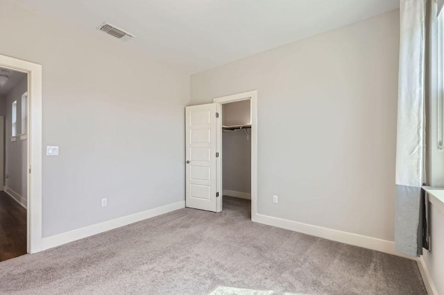 unfurnished bedroom with visible vents, carpet flooring, a walk in closet, and baseboards