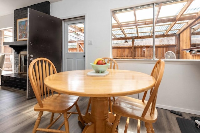 dining area featuring a large fireplace, baseboards, and wood finished floors