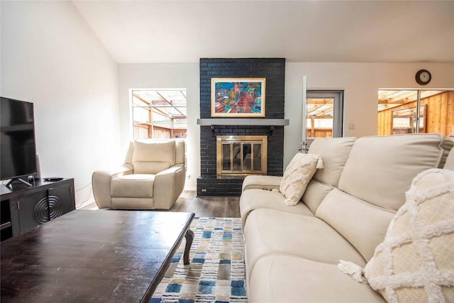 living room with vaulted ceiling, a brick fireplace, and wood finished floors