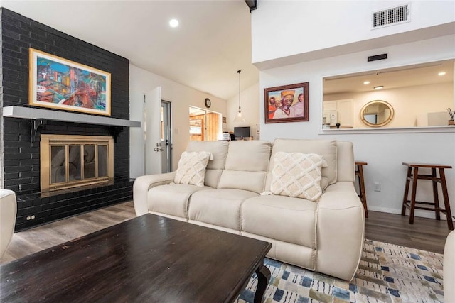 living room with baseboards, visible vents, wood finished floors, vaulted ceiling, and a brick fireplace