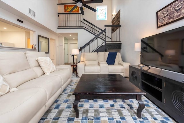 living area featuring stairs, a high ceiling, visible vents, and a ceiling fan