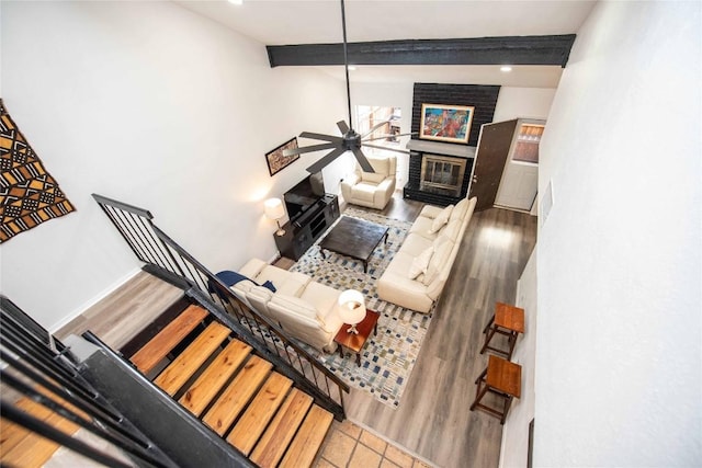 living room featuring beam ceiling, stairway, a brick fireplace, wood finished floors, and baseboards