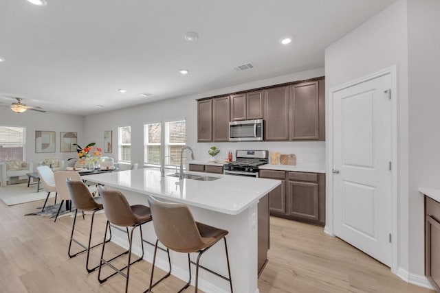 kitchen featuring a breakfast bar area, stainless steel appliances, light countertops, light wood-type flooring, and a sink