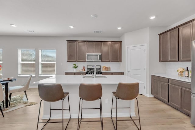 kitchen featuring stainless steel appliances, light countertops, a kitchen island with sink, a sink, and a kitchen bar