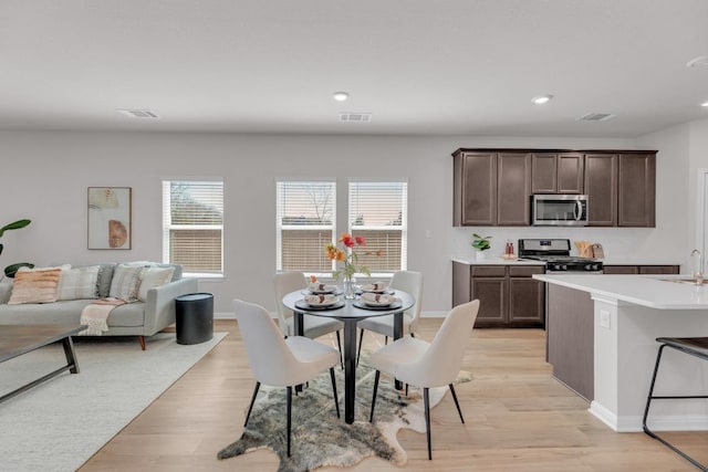 kitchen with a sink, light countertops, appliances with stainless steel finishes, dark brown cabinets, and light wood finished floors