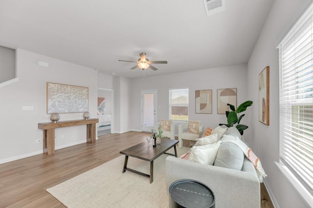 living room with light wood-type flooring, visible vents, baseboards, and a ceiling fan