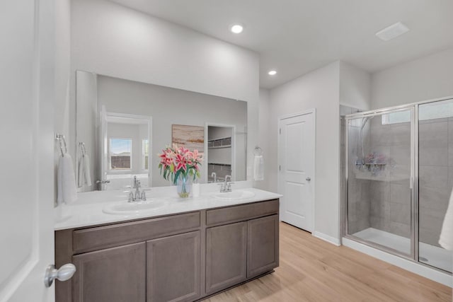 full bath featuring a stall shower, double vanity, a sink, and wood finished floors