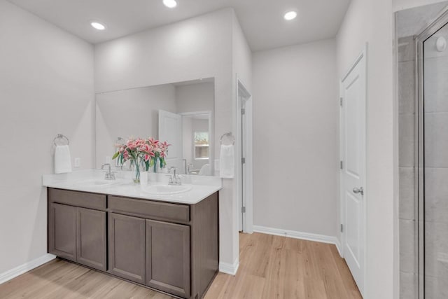 full bath featuring double vanity, wood finished floors, a sink, and baseboards