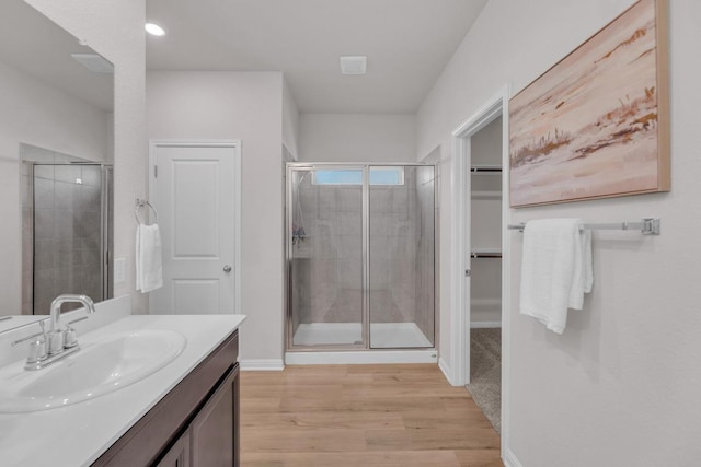 full bath with wood finished floors, vanity, baseboards, a shower stall, and a walk in closet