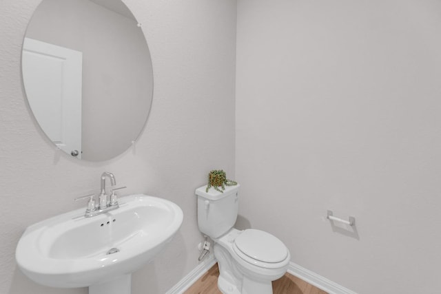 half bath with wood finished floors, a sink, toilet, and baseboards