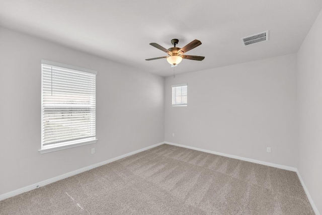 empty room with carpet floors, a ceiling fan, visible vents, and baseboards