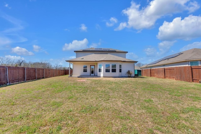 back of property with roof mounted solar panels, a fenced backyard, a lawn, and a patio