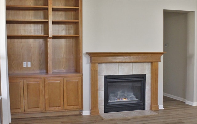 unfurnished living room with a tile fireplace, baseboards, and wood finished floors