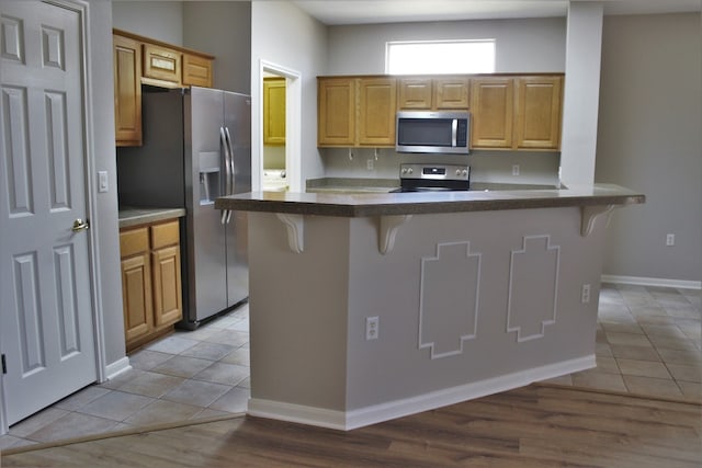 kitchen featuring light tile patterned floors, a breakfast bar area, baseboards, appliances with stainless steel finishes, and dark countertops