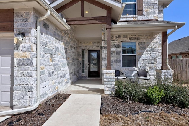 entrance to property featuring an attached garage, stone siding, and covered porch