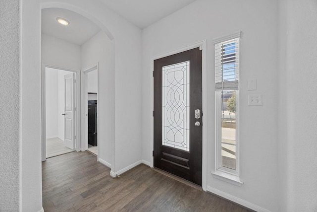 foyer with arched walkways, dark wood-type flooring, and baseboards