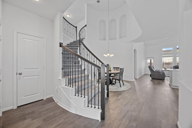 staircase featuring a chandelier, arched walkways, wood finished floors, a towering ceiling, and baseboards