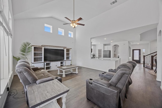 living area with arched walkways, visible vents, wood finished floors, high vaulted ceiling, and stairs