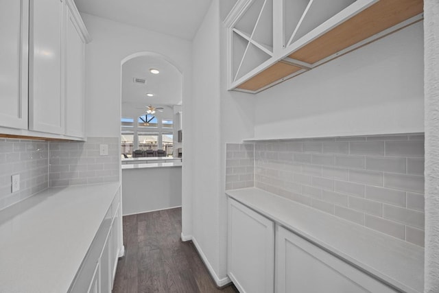 interior space with tasteful backsplash, arched walkways, white cabinets, ceiling fan, and dark wood-style flooring