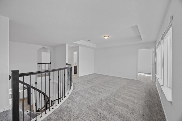 corridor with an upstairs landing, baseboards, a tray ceiling, and light colored carpet