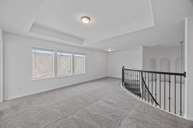 spare room with carpet floors, a raised ceiling, and baseboards