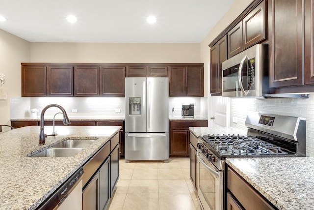 kitchen with light tile patterned flooring, light stone countertops, stainless steel appliances, and a sink