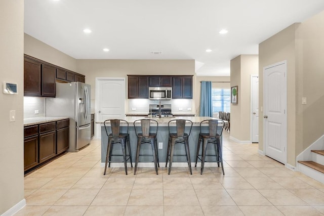 kitchen featuring a breakfast bar, tasteful backsplash, stainless steel appliances, light tile patterned floors, and dark brown cabinets